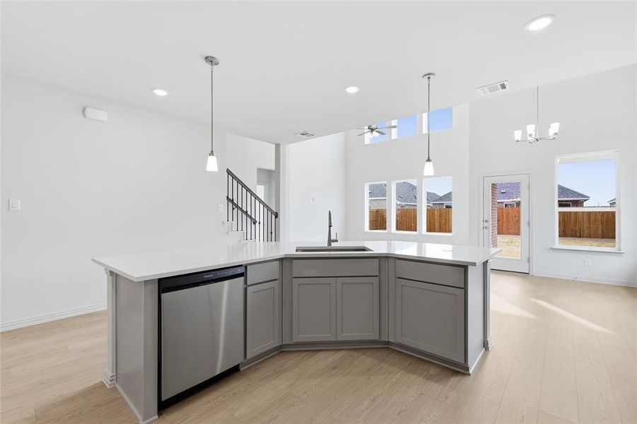 Kitchen featuring an island with sink, gray cabinets, dishwasher, light wood finished floors, and a chandelier