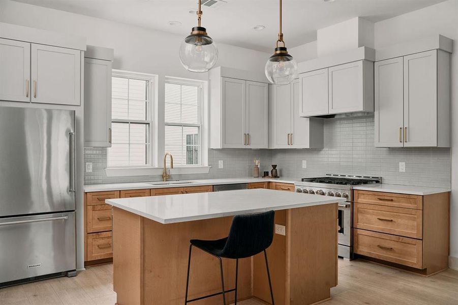 Modern kitchen featuring a light wood-finish island with a white countertop and a stainless steel appliance suite Modern kitchen featuring a light wood-finish island with a white countertop and a stainless steel appliance suite