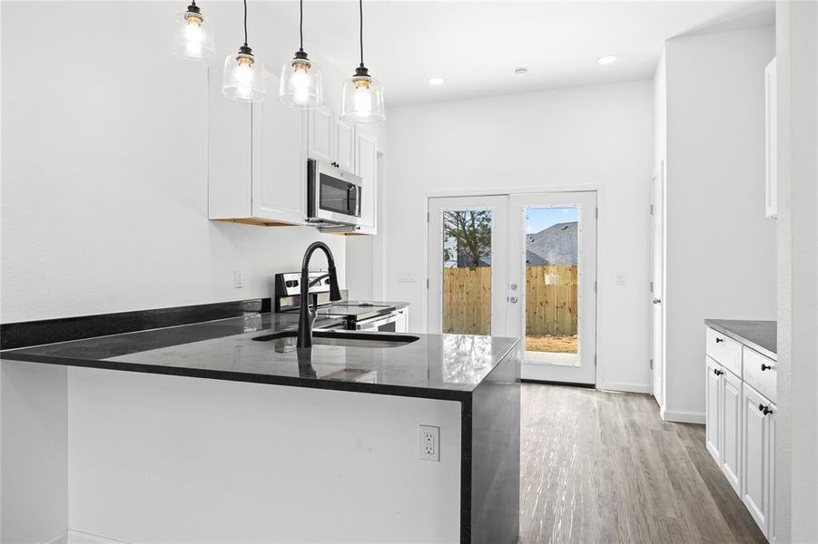 Kitchen featuring kitchen peninsula, white cabinetry, pendant lighting, and appliances with stainless steel finishes