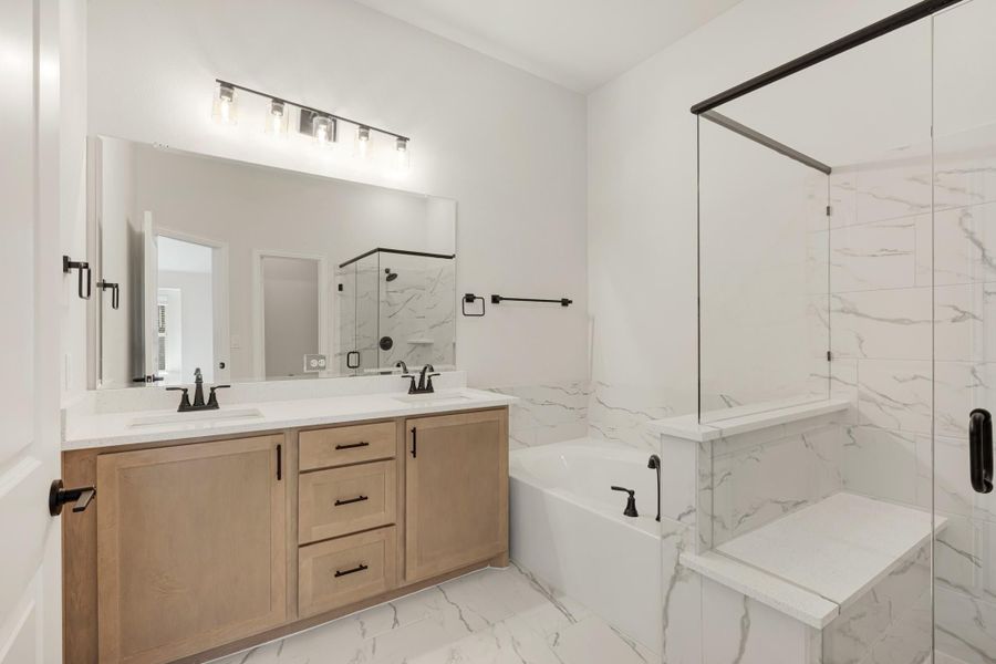 Bathroom with double vanity, wood cabinets, soaking tub, and glass shower with white marble tile