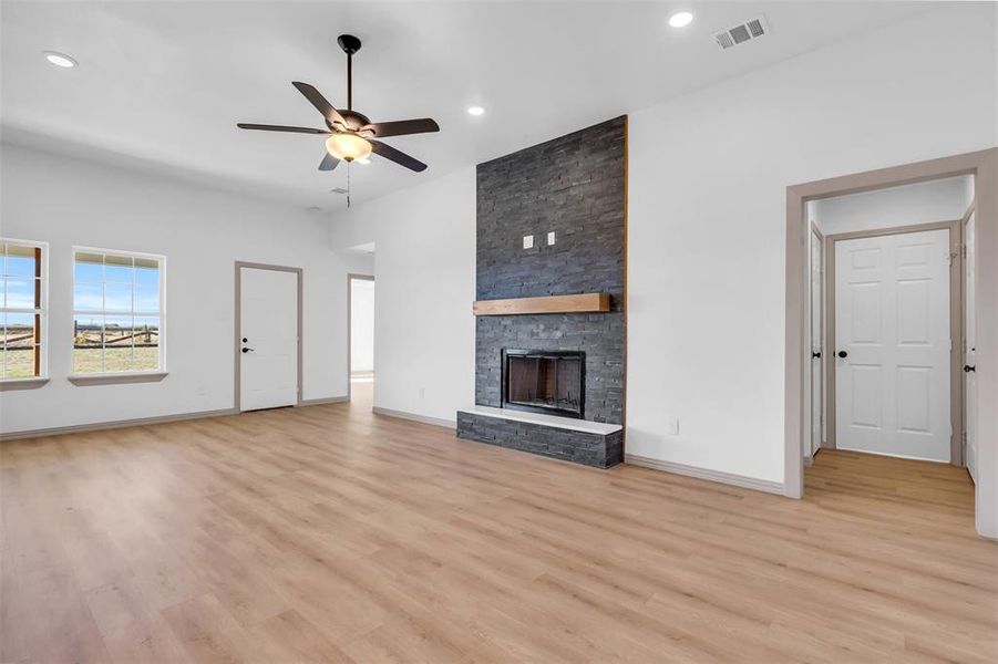 Unfurnished living room with ceiling fan, a stone fireplace, and light hardwood / wood-style flooring