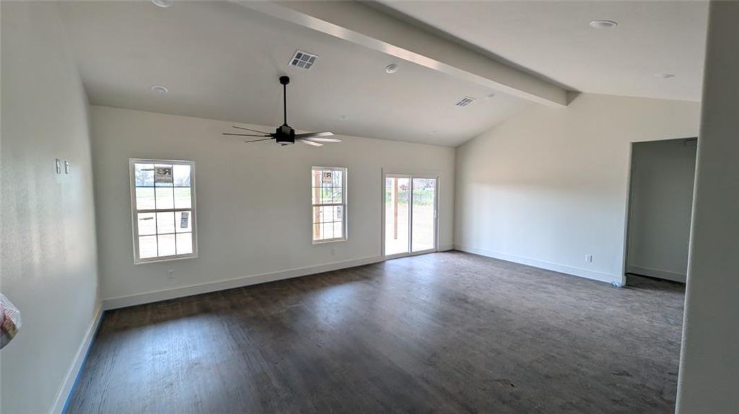 Spare room featuring a ceiling fan, dark wood-style floors, visible vents, baseboards, and vaulted ceiling with beams