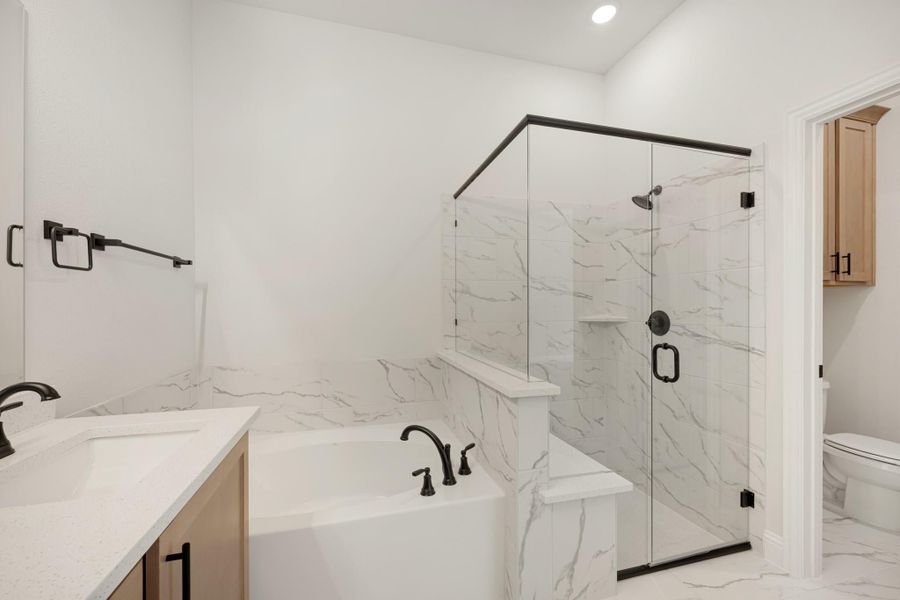 Master bathroom with marble tile, soaking tub, glass walk-in shower, and light wood vanity cabinets