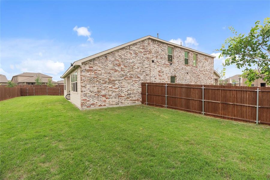 Expansive green lawn bordering a brick and siding exterior, featuring multiple windows and a privacy fence