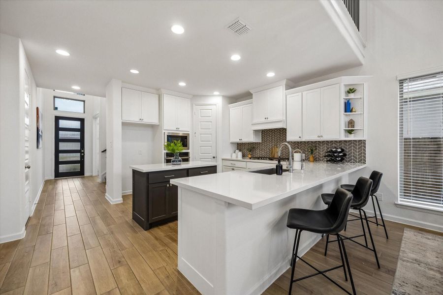 The kitchen keeps daily life easy with a large island, quartz countertops, crisp white cabinetry, sleek stainless-steel appliances, and plenty of room for prep, serving, and gathering. Bar seating creates a casual spot for coffee, snacks, or conversation while staying connected to the open dining and living areas.