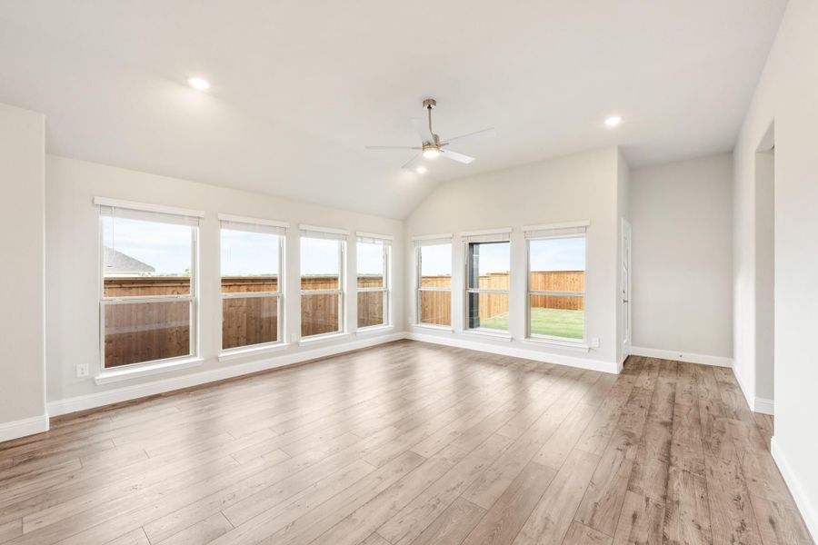 Empty living room with vaulted ceiling, ceiling fan, hardwood floors, and large windows overlooking backyard Empty living room with vaulted ceiling, ceiling fan, hardwood floors, and large windows overlooking backyard