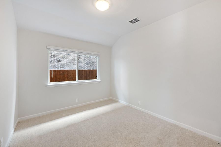 Empty bedroom with vaulted ceiling, carpet flooring, and a single window with backyard view