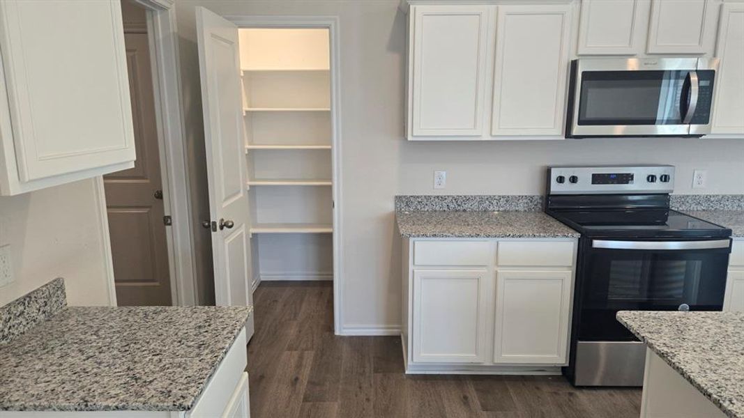 Kitchen with appliances with stainless steel finishes, light stone countertops, white cabinetry, and dark wood-type flooring