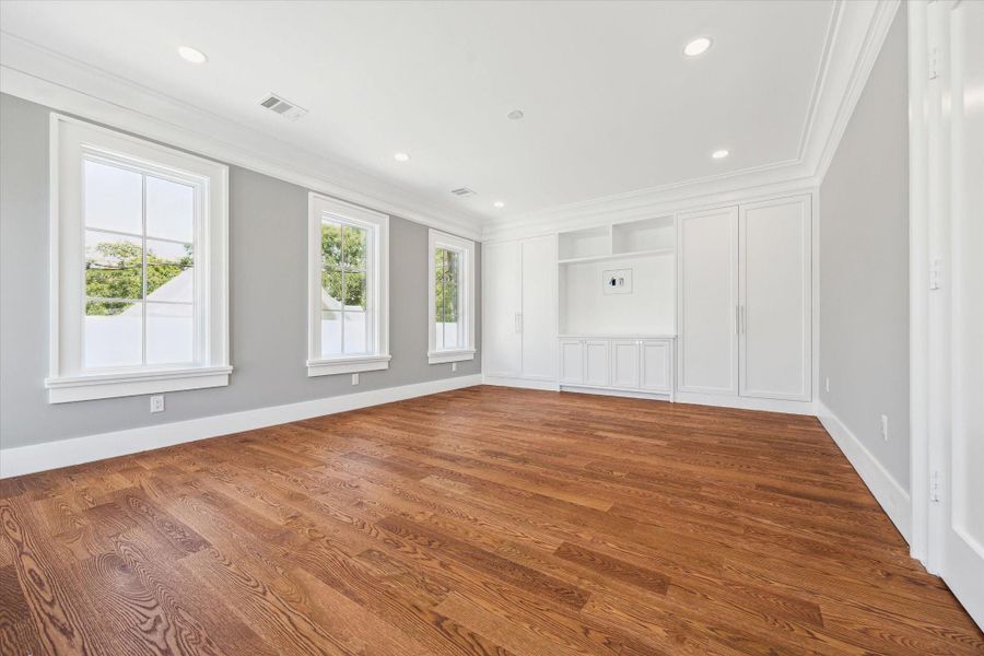 Another view of this 2nd floor bedroom that features hardwood floors, abundant natural light from three large windows, and built-in white cabinetry for storage. The neutral gray walls and recessed lighting create a modern and inviting atmosphere.  This is the room that opens to the balcony.