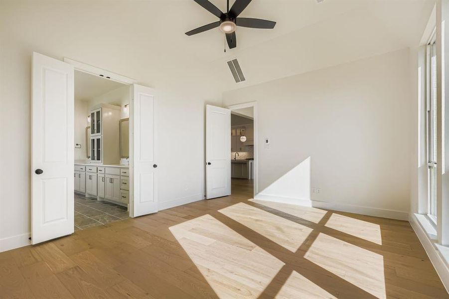 Unfurnished bedroom featuring light wood-type flooring, a ceiling fan, and connected bathroom