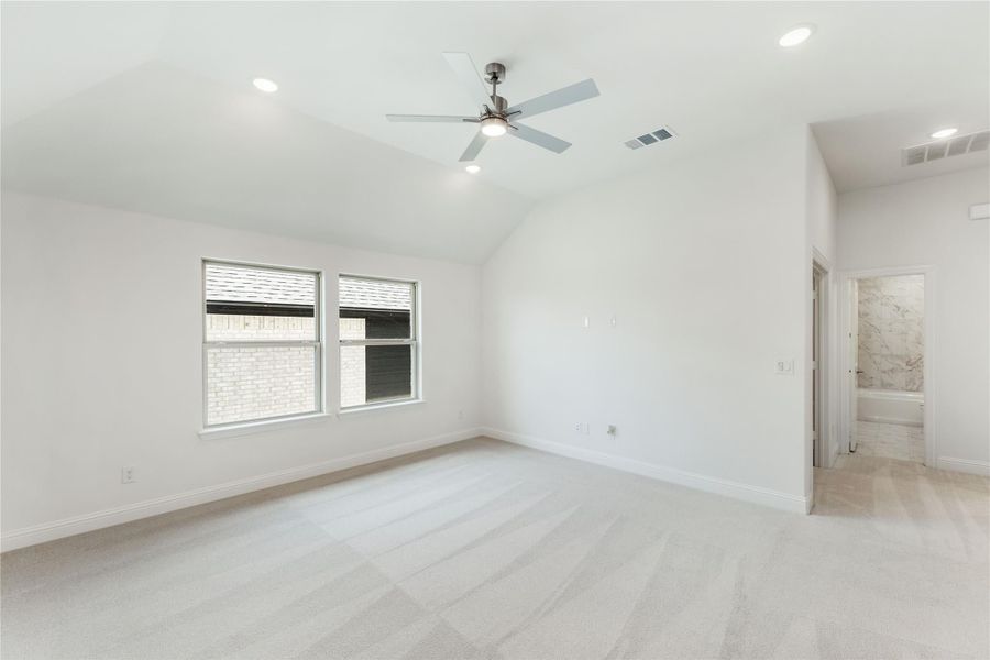 Empty master bedroom with vaulted ceiling, ceiling fan, carpet flooring, and ensuite bathroom entrance