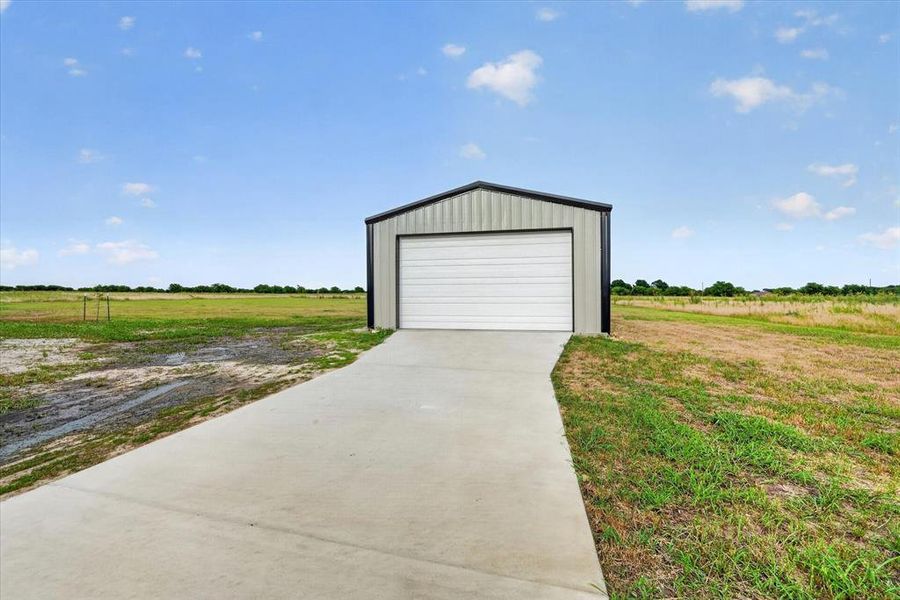 Detached metal structure featuring a white sectional garage door, gray corrugated siding, and a dark trim roofline
