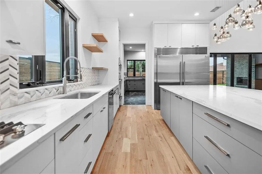 Modern kitchen featuring light wood-finish flooring, white upper cabinetry, and a large island with a light-colored countertop Modern kitchen featuring light wood-finish flooring, white upper cabinetry, and a large island with a light-colored countertop