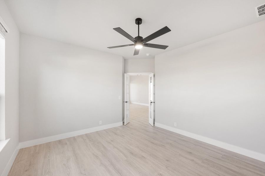 Empty bedroom with light wood floors, white walls, black ceiling fan, and open doorway Empty bedroom with light wood floors, white walls, black ceiling fan, and open doorway