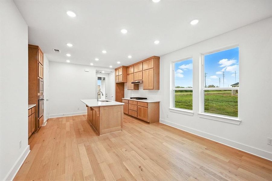 Kitchen with a center island with sink, light wood-style flooring, recessed lighting, stainless steel oven, and brown cabinetry Kitchen with a center island with sink, light wood-style flooring, recessed lighting, stainless steel oven, and brown cabinetry