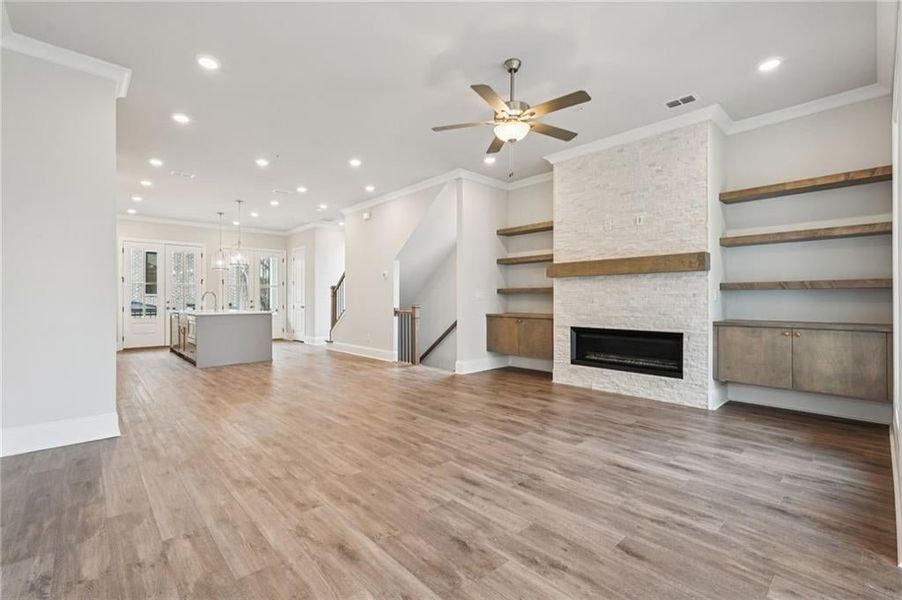 Unfurnished living room with recessed lighting, a stone fireplace, crown molding, light wood finished floors, and ceiling fan