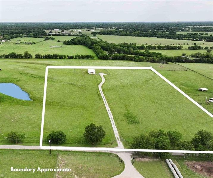 Expansive land parcel featuring a residential structure, a distinct pond, a winding driveway, and mature trees
