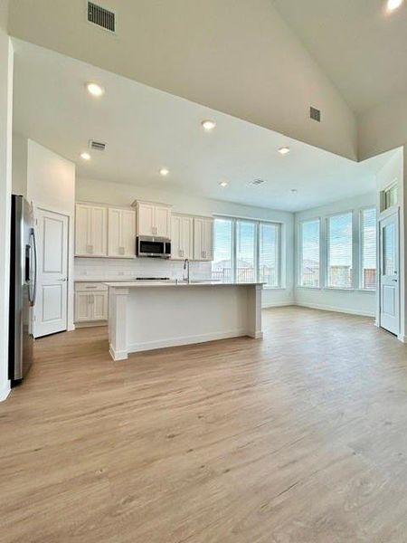 Open-concept living space featuring wood-finish flooring, a kitchen island with seating, stainless steel appliances, white cabinetry, and multiple large windows