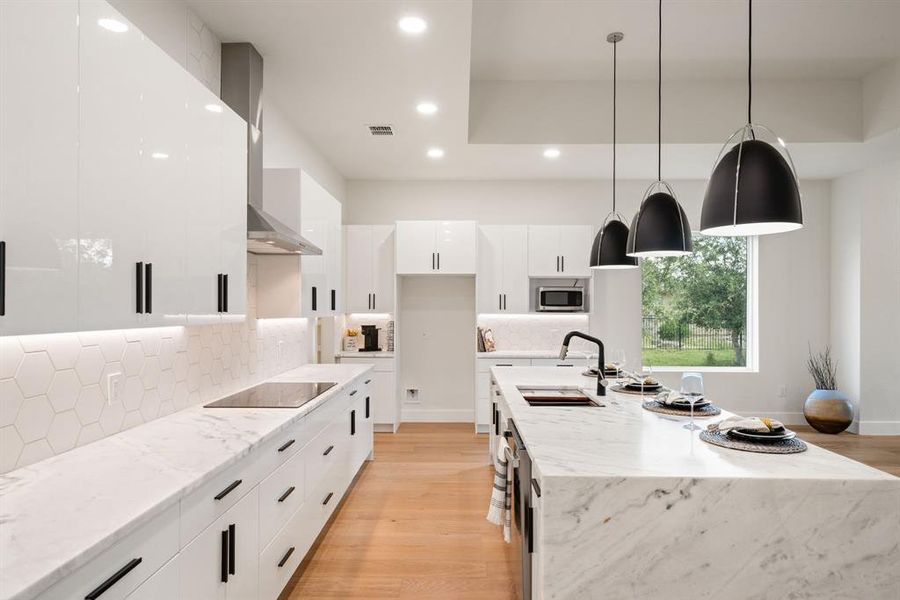 Kitchen featuring light stone counters, white cabinets, backsplash, light wood-style flooring, and pendant lighting