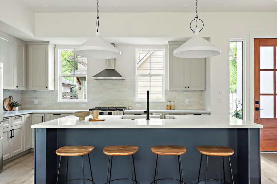 Kitchen with a sink, light countertops, backsplash, and wall chimney range hood