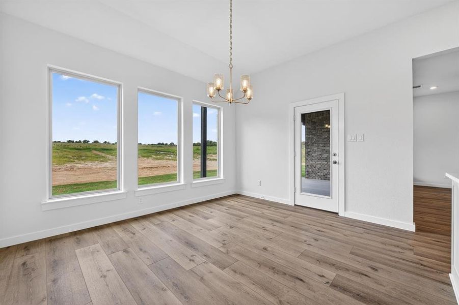 Spacious room featuring three large picture windows, wood-finish flooring, a modern chandelier with frosted glass shades, a glass-paneled door, and clean white walls