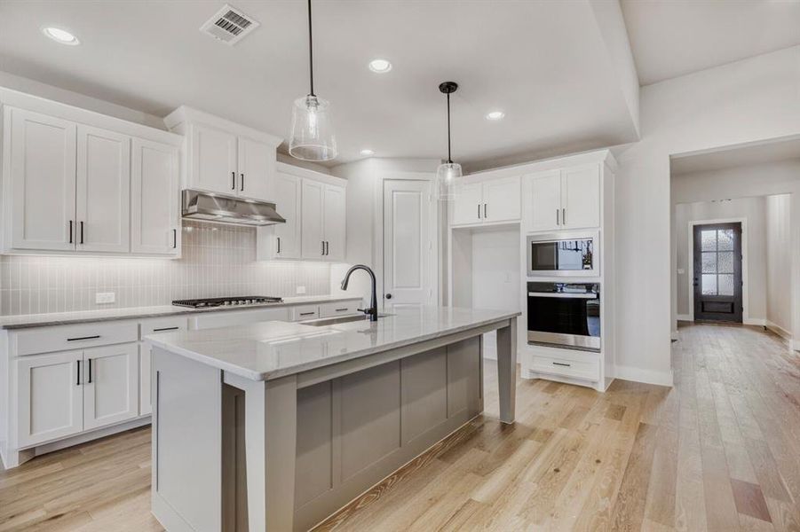 Kitchen with stainless steel appliances, light wood-style flooring, an island with sink, and light stone countertops