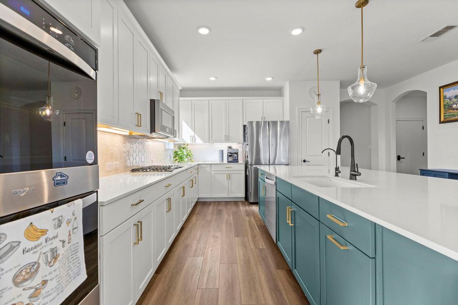Kitchen with stainless steel appliances, tasteful backsplash, decorative light fixtures, two tone cabinetry, and arched walkways