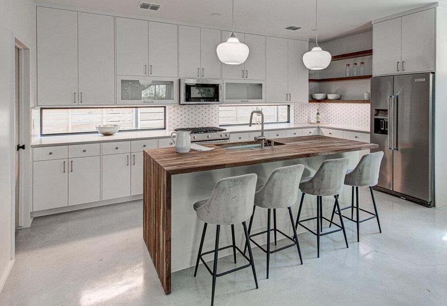 Kitchen featuring finished concrete flooring, open shelves, stainless steel appliances, butcher block counters, and a sink