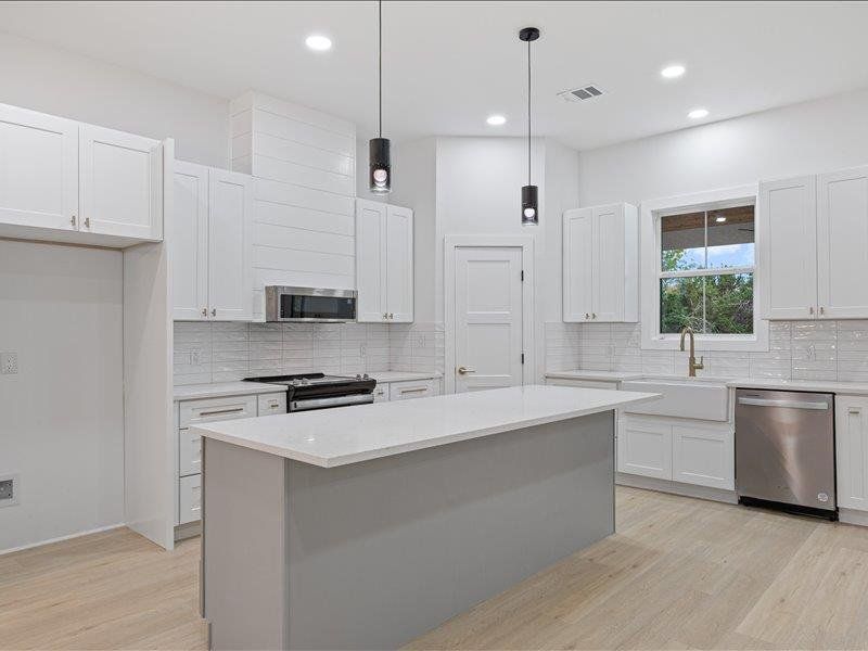 The kitchen features white cabinetry, a large central island with a light-colored countertop, and light wood flooring