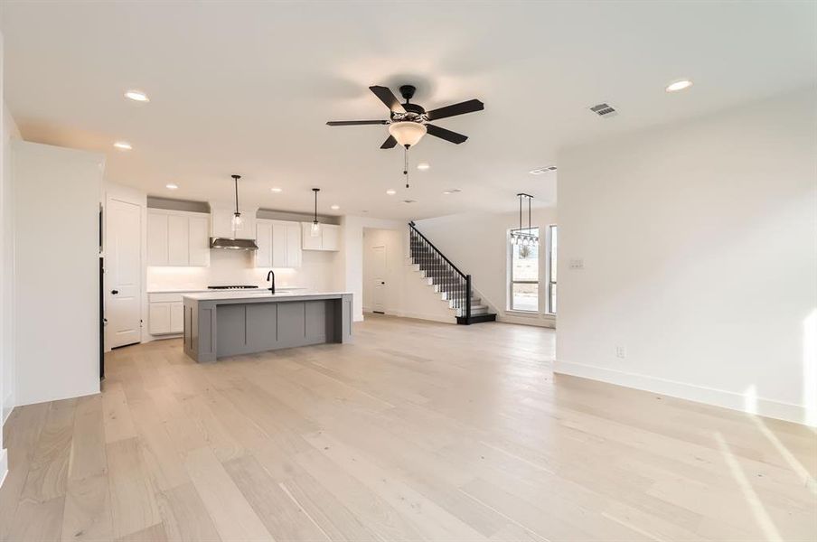 Kitchen featuring white cabinetry, ceiling fan, hanging light fixtures, light hardwood / wood-style flooring, and a center island with sink