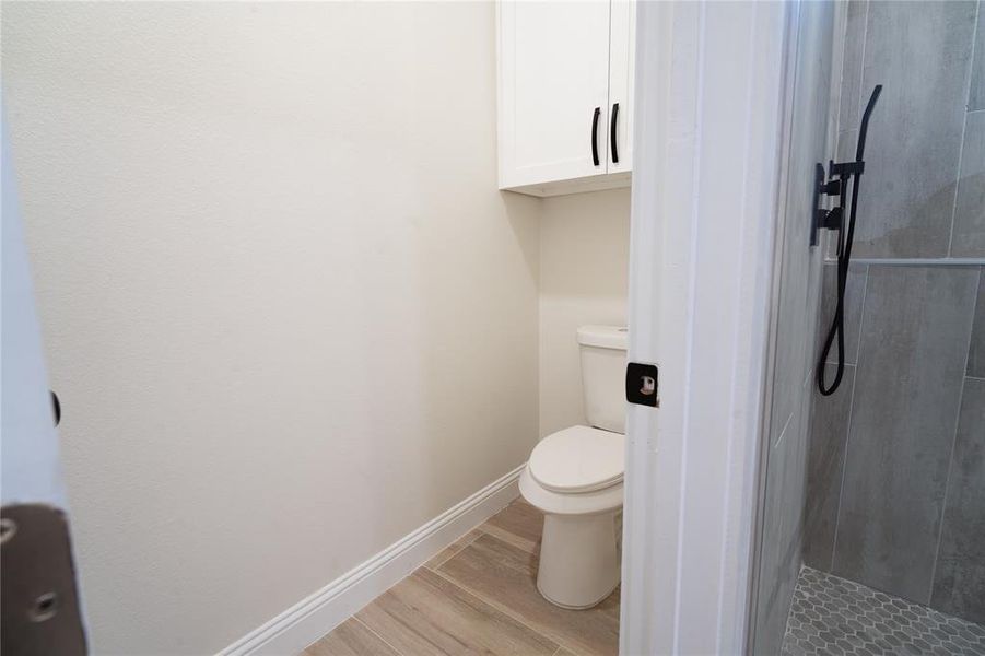 Full bath featuring toilet, a shower stall, baseboards, and wood finished floors