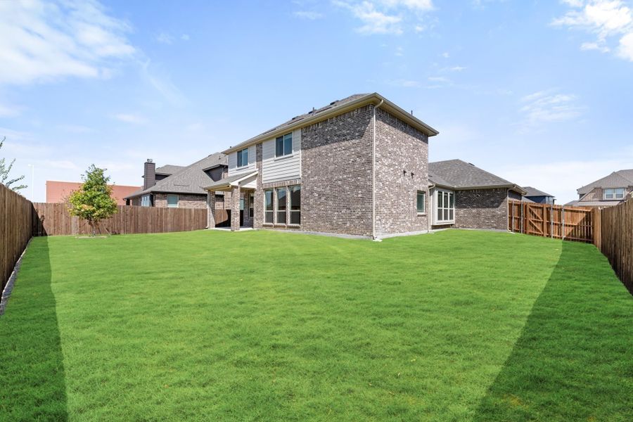 Two-story brick home with large grassy backyard enclosed by wood privacy fence
