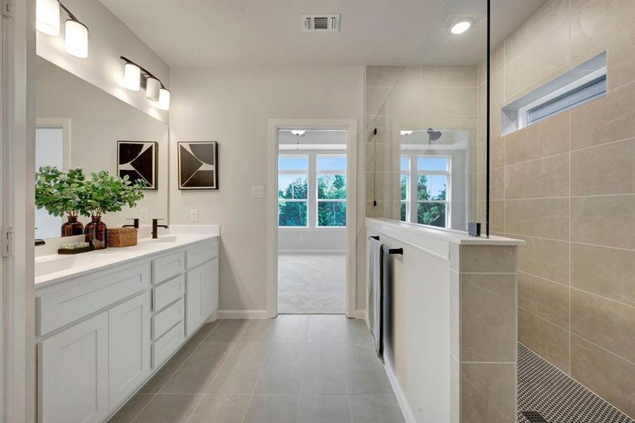 Spacious bathroom featuring a double vanity with white cabinetry, a large frameless shower with tile walls, and a window for natural light