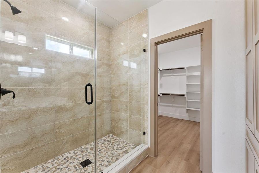 Full bath featuring a shower stall, a spacious closet, and light wood-type flooring Full bath featuring a shower stall, a spacious closet, and light wood-type flooring