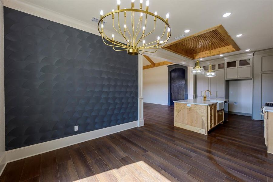 Two tone kitchen featuring an island with sink, dark wood finished floors, open floor plan, an accent wall, and glass insert cabinets