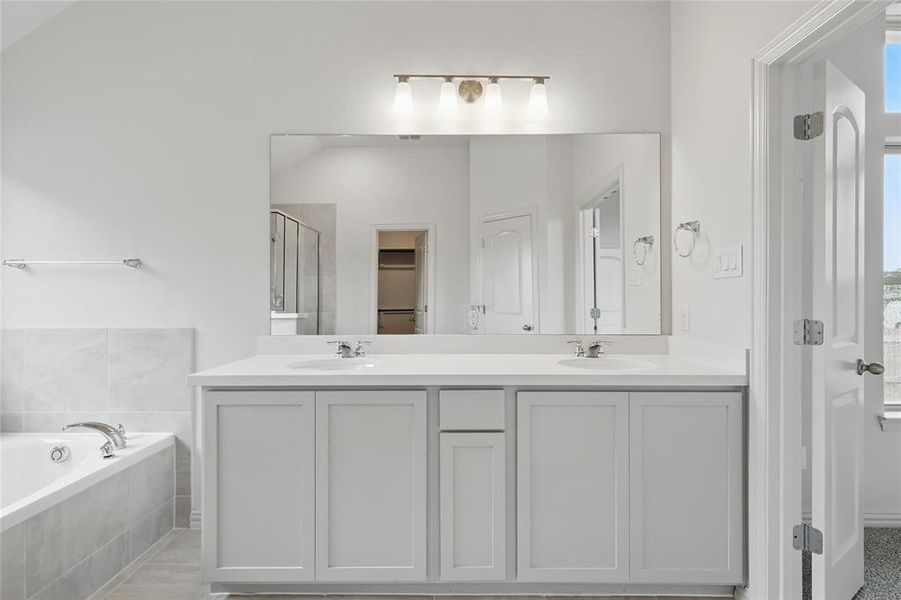 Full bathroom featuring double vanity, a garden tub, a stall shower, and a walk in closet