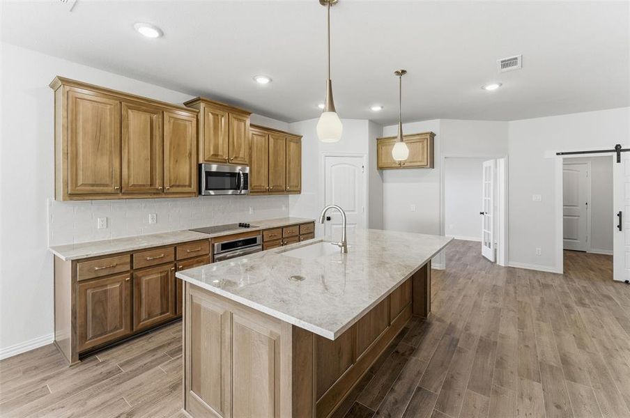 Kitchen with wood finish cabinetry, a barn door, light stone counters, light wood finished floors, and decorative backsplash
