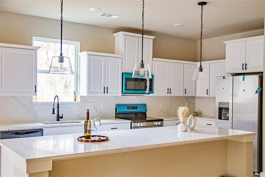 Kitchen featuring white cabinets, decorative light fixtures, appliances with stainless steel finishes, and light stone counters