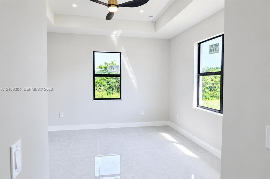 Room featuring neutral tile flooring, a tray ceiling, recessed lighting, a modern ceiling fan, and black-framed windows