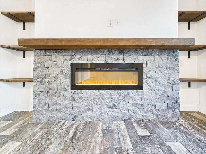 Close up of modern linear electric fireplace set in a stacked-stone surround. Built-in floating wood shelves on each side provide display and storage options.