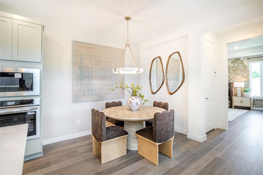 This is a modern dining area featuring a round table with upholstered chairs, a stylish pendant light, and contemporary decor. The space is adjacent to a kitchen with built-in appliances and opens into a living area with large windows. This is a modern dining area featuring a round table with upholstered chairs, a stylish pendant light, and contemporary decor. The space is adjacent to a kitchen with built-in appliances and opens into a living area with large windows.