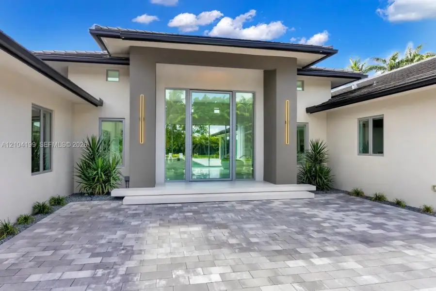 Modern architectural exterior featuring a paved stone driveway, recessed entry with a double-height frame, full-height glass entryway, and vertical wall-mounted lighting