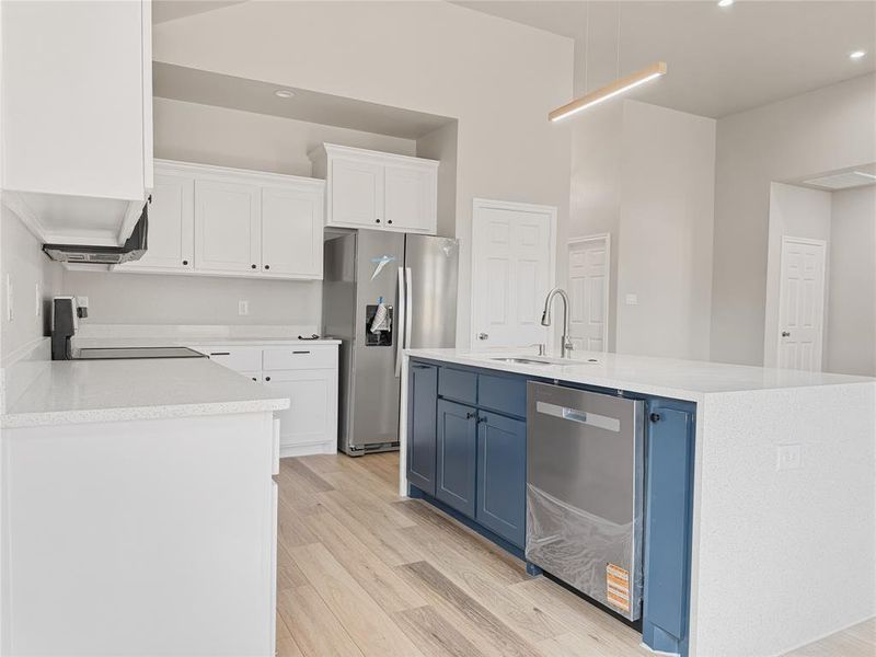 Dual tone kitchen with two tone cabinetry, stainless steel appliances, light wood-style floors, light stone countertops, and a center island with sink
