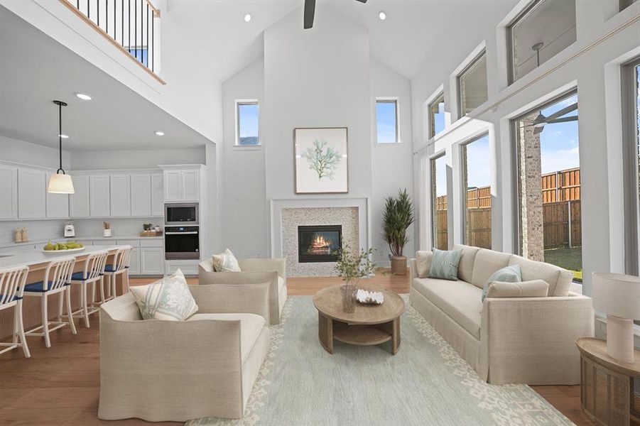 Living room featuring high vaulted ceiling, healthy amount of natural light, recessed lighting, a glass covered fireplace, and light wood-style flooring