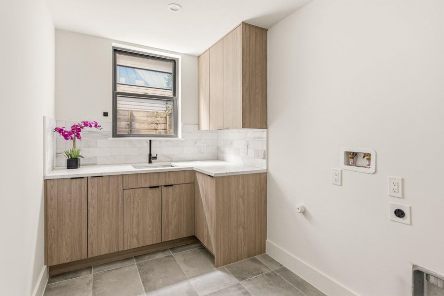 Utility room featuring light wood-finish cabinetry, white countertop, and a tile backsplash