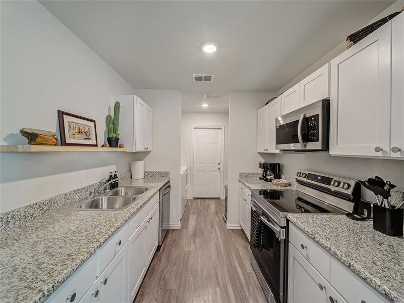 Kitchen with stainless steel appliances, white cabinets, light stone countertops, light wood finished floors, and open shelves