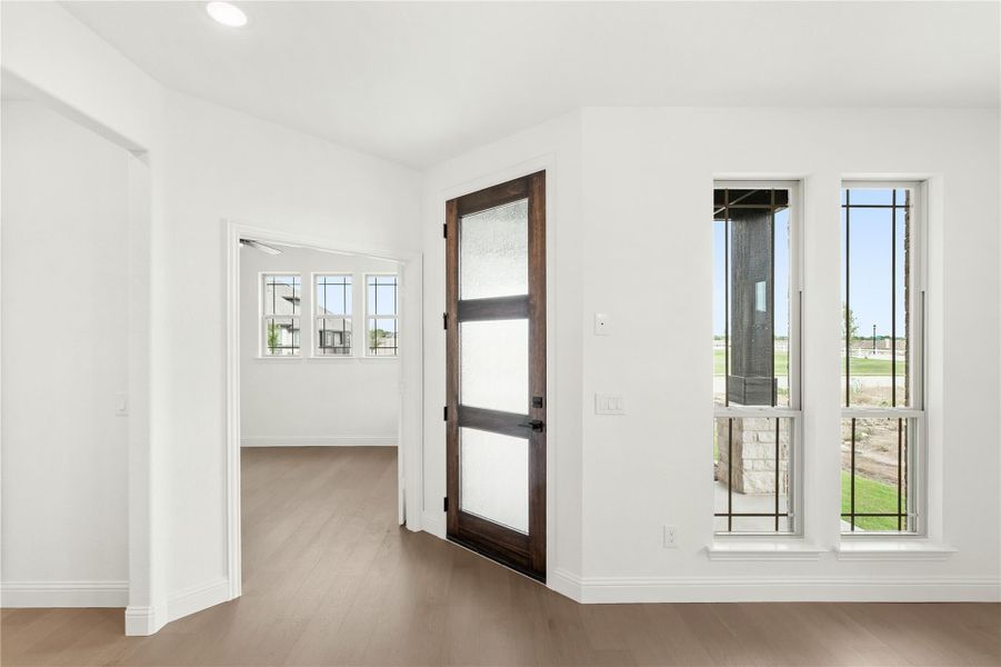 Entryway with dark wood glass-panel door, white walls, and light hardwood floors Entryway with dark wood glass-panel door, white walls, and light hardwood floors