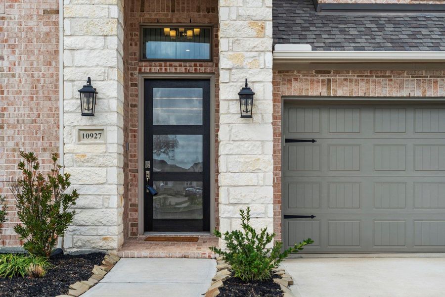 Sophisticated stone and brick facade featuring a contemporary glass-panel door, designer coach lighting, and professional landscaping. Sophisticated stone and brick facade featuring a contemporary glass-panel door, designer coach lighting, and professional landscaping.