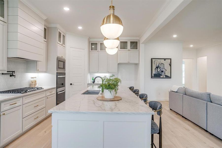 Kitchen featuring custom cabinetry to the ceiling, light hardwood floors, large island with Quartzite countertops, and beautiful hardware.