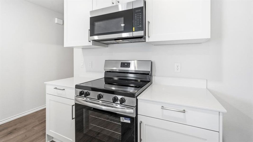 Kitchen featuring stainless steel appliances, white cabinets, and dark wood-style floors Kitchen featuring stainless steel appliances, white cabinets, and dark wood-style floors